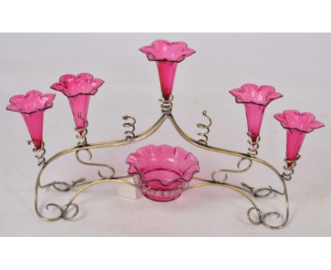 An Edwardian silver plated scrolling wirework framed epergne set with five cranberry tinted flared vases and central bowl, le