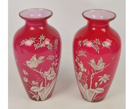 A pair of Victorian white enamel overlaid and dark pink tinted glass vases, each decorated with a bird amongst floral and lea