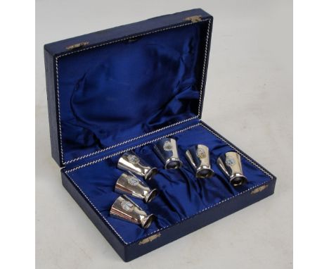 A cased set of six Kuwaiti souvenir shot cups of tapering form, each applied with shield shaped enamel plaque, silver standar