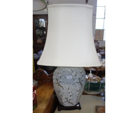 A CHINESE STYLE GLAZED CERAMIC TABLE LAMP decorated with blossoms on a grey ground on a wooden effect stand, cream coloured s