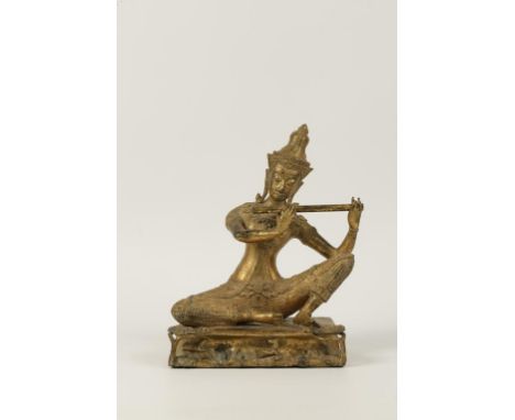 A THAI GILT BRONZE FIGURE OF A FLUTE PLAYING DEITY, the jewelled figure wearing a crown, on shaped rectangular dais, with nat