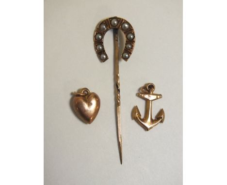 A 9 CT GOLD ANCHOR SHAPED CHARM TOGETHER WITH A HEART SHAPED EXAMPLE AND A YELLOW METAL HORSESHOE AND SEED PEARL STICK PIN (3