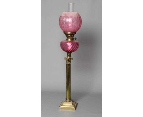 A VICTORIAN BRASS CORINTHIAN COLUMN OIL LAMP with etched cranberry spherical shade and clear chimney issuing from a wrythen m