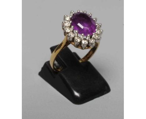 AN AMETHYST AND DIAMOND CLUSTER RING, the oval facet cut amethyst claw set to a border of fourteen small brilliant cut diamon