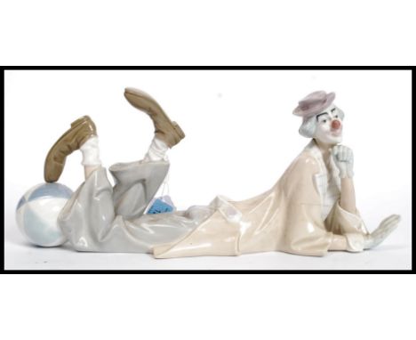 A large Lladro figure of a clown in repose leaning with his foot resting on a large circus ball. Believed model no 4618. L37 