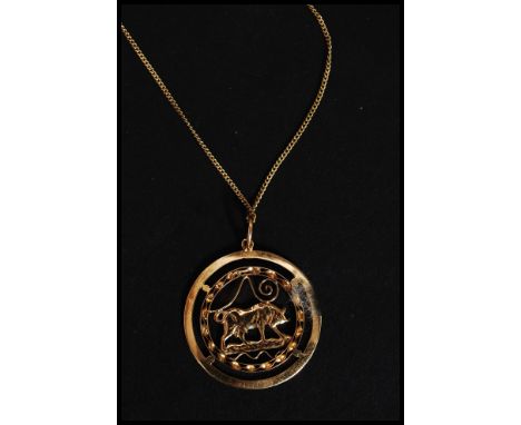 An 18ct gold pendant necklace. The round and pierced pendant with bull to centre and ribbon work surround. Set to a fine chai