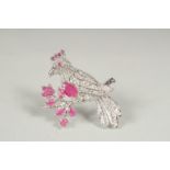 A silver and ruby set bird brooch in a box.