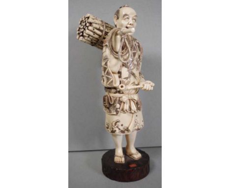 1920s Japanese ivory okimono of a woodsman carrying a bundle of sticks supported by a pole on his shoulder and holding a pipe