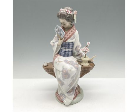 Glossy figurine modeled as a demure Japanese woman with a fan seated on a bench with bird and flowers. Lladro backstamp. This