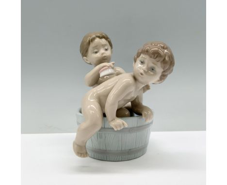 Two children happily bathing together in a wooden tub, one gently scrubbing the other's back. Lladro backstamp. This item has