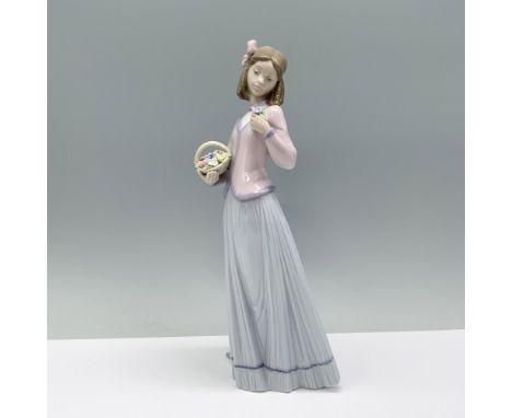 A woman elegantly dressed in a pink blouse and lavender skirt gracefully holds a basket of flowers in one hand and a bouquet 