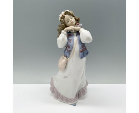 A young girl in a white dress and denim vest delicately holds her hands to her chin, crowned with a wreath of flowers. Lladro