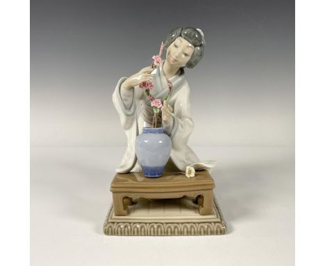 A Japanese Geisha in a pristine white robe delicately arranging flowers in a vase. Lladro backstamp. This item has its origin
