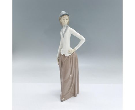 Glazed porcelain figure of a lady standing in a grey hat, white top and dusty pink skirt with one hand on her hip. Nao backst