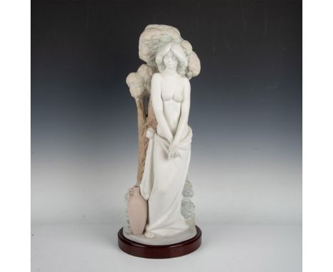 A lovely figure of a beauty topless in a long cloth skirt. She is depicted standing in front of a tree, her left hand gracefu