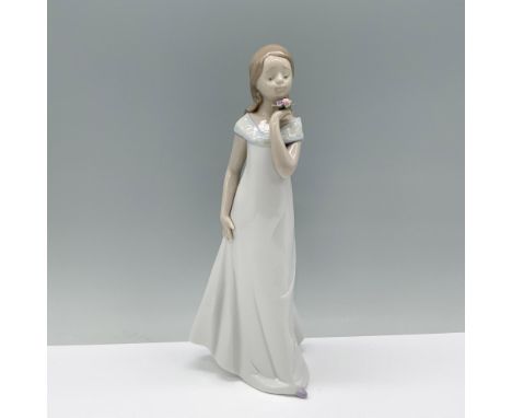 The woman in the flowing white dress strikes a graceful pose, gently admiring a small bouquet of flowers in her hand. Lladro 
