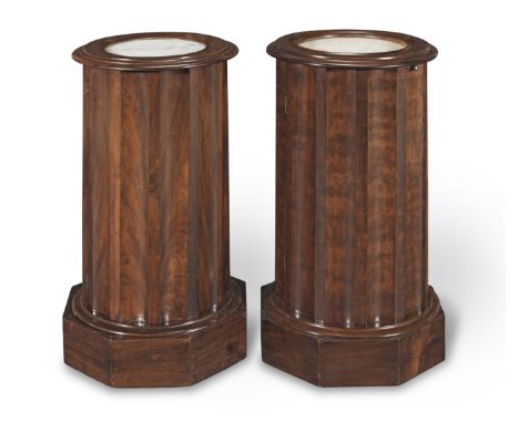 A pair of mahogany column-form bedside cabinetsEach with a circular marble top within a moulded surround, above a fluted body