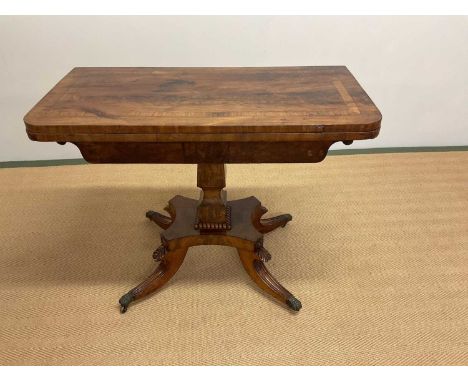 An early 19th century mahogany crossbanded card table with quadripartite base and four acanthus carved outswept legs to brass