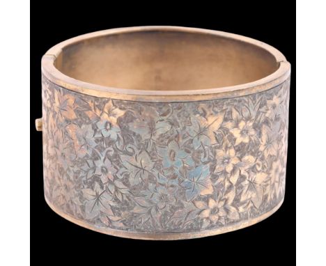 A Victorian silver-gilt hinged bangle, maker J&THF, Birmingham 1883, engraved floral decoration, band width 39mm, internal ci