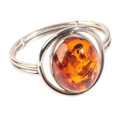 A CONTEMPORARY AMBER BANGLEin sterling silver, set with an amber cabochon of 39x30x16mm, c.54.59 carats, held in a bezel sett