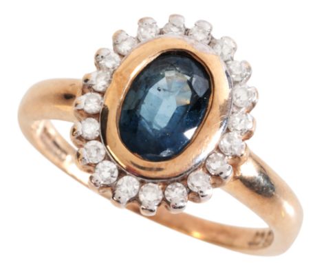 A SAPPHIRE AND DIAMOND CLUSTER RINGin low carat gold, set with an oval cut sapphire of c.1.06 carats, held in a bezel setting