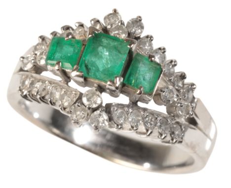 AN EMERALD AND DIAMOND DRESS RINGin white gold, set centrally with three graduating step cut emeralds totalling c.0.60 carats