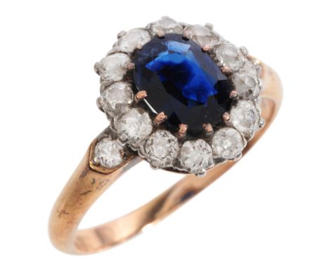 AN ANTIQUE SAPPHIRE AND DIAMOND CLUSTER RING in 18ct gold and platinum, set with an oval cut sapphire of c.1.10 carats, surro