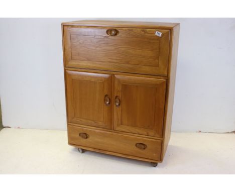 Ercol Windsor Blonde Elm Cocktail Cabinet, with fall front above two cupboards and a long drawer raised on castors, 110cms hi