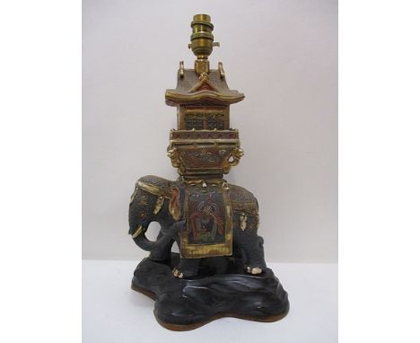 An early 20th century Satsuma table lamp fashioned as an elephant with a howdah and building on its back, on a carved wood st