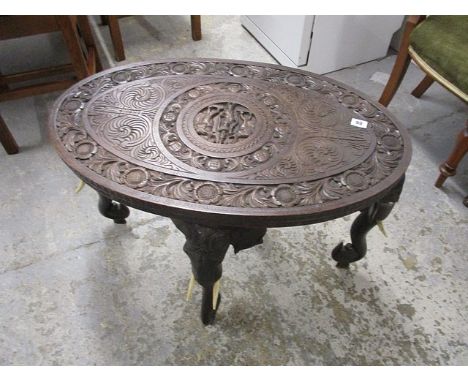 An early 20th century Indian carved hardwood occasional table, the oval top decorated with figures, elephants and flora, on e