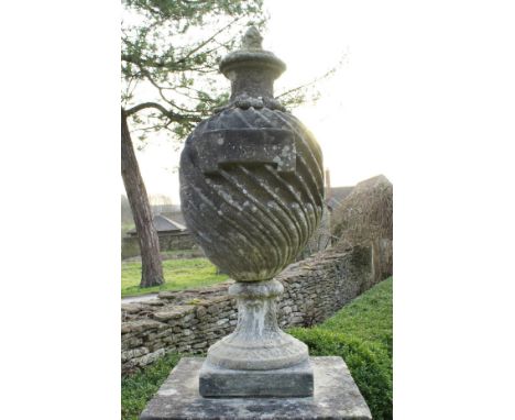 A carved reconstituted stone garden urn or finial of wrythen stop fluted form, raised on a heavy plinth base in the Georgian 