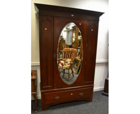 An early-20th century mahogany double wardrobe, outswept cornice above oval mirrored door, flanked by elongated arched panels