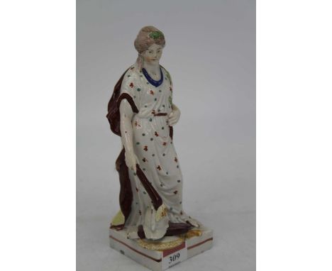 A 19th century Staffordshire pearlware figure of Peace in standing pose with flaming torch in right hand, upon a helmet with 