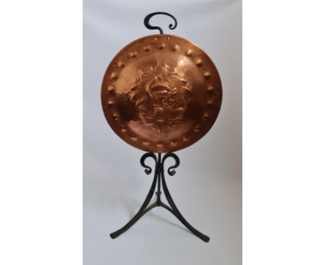An arts and crafts copper fire screen on cast iron tripod base with dragon design.
