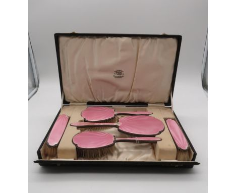 Hamilton &amp; Inches; A cased five piece pink guilloche enamel dressing table set, comprising two hair brushes, two clothes 