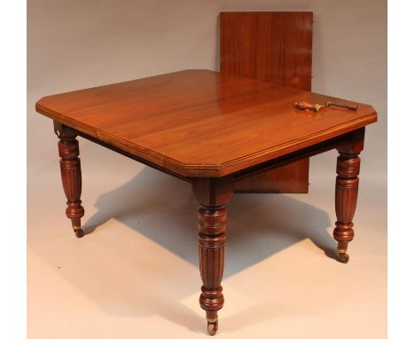 A late Victorian walnut dining table, the plain top with canted corners raised on carved supports terminating in castors, wit