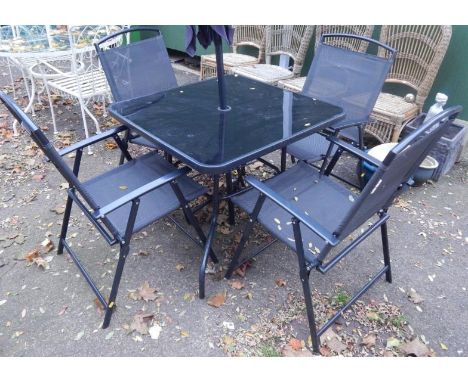 A black metal patio set, comprising square table with glass top, four folding chairs and a parasol.