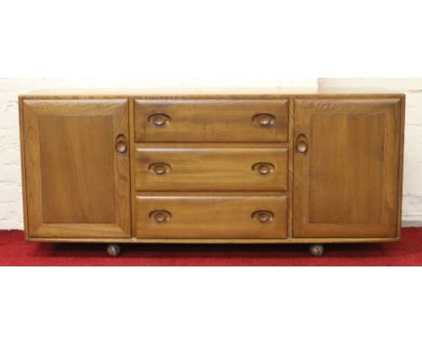 An Ercol light elm sideboard of three drawers flanked by cupboards.