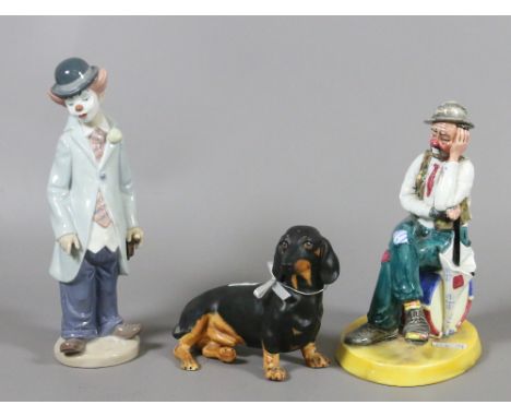A Coalport figurine 'Woeful Tramp' along with a Coalport model of a dachshund and Lladro figurine of a child clown (AF).