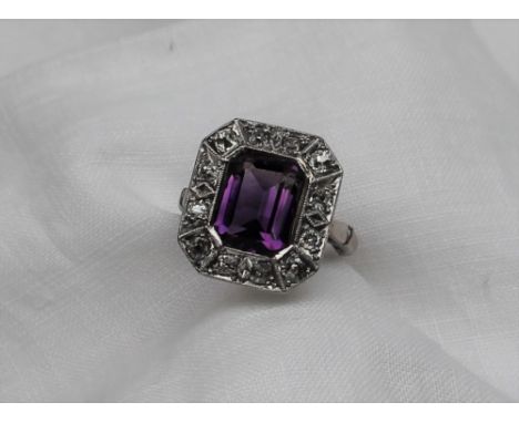 An amethyst and diamond ring, the central emerald cut amethyst measuring 10mm x 8mm surrounded by twelve rose cut diamonds to