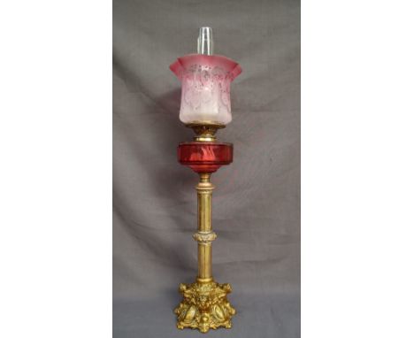 A Victorian brass and gilt metal oil lamp, with an etched graded glass shade and a cranberry glass reservoir, the base cast w