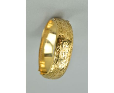 A 9CT GOLD HINGED BANGLE, the front half engraved with scrolling acanthus leaf decoration to the push piece clasp, hallmarked