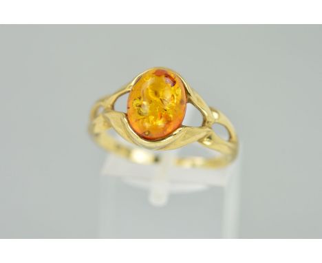 A 9CT GOLD MODIFIED AMBER RING, designed as an oval modified amber cabochon to the tapered openwork shoulders, hallmark for L