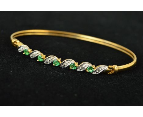 A 9CT GOLD EMERALD AND DIAMOND BANGLE, designed as five circular emeralds interspaced by leaf shape panels each set with sing