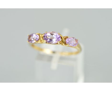 A 9CT GOLD AMETHYST RING designed as three claw set graduated oval amethysts interspaced by curved cross detail, hallmarked B