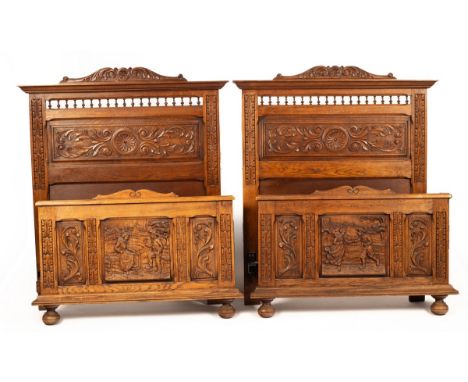 A pair of late 19th Century oak single bedsteads with leaf and scroll carved headboards, the footboards carved bucolic scenes