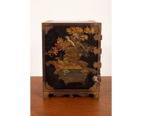 A Japanese black and gold lacquer cabinet, with engraved brass mounts, enclosed by a door decorated flowers in a planter rais