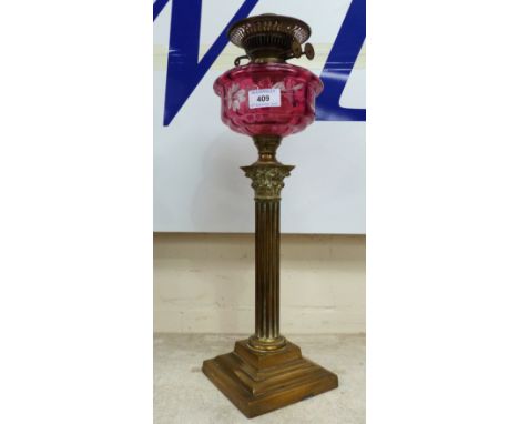 A Victorian oil lamp with reeded brass column, stepped base and cranberry glass reservoir
