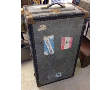 A large vintage grey travelling trunk with destination labels.