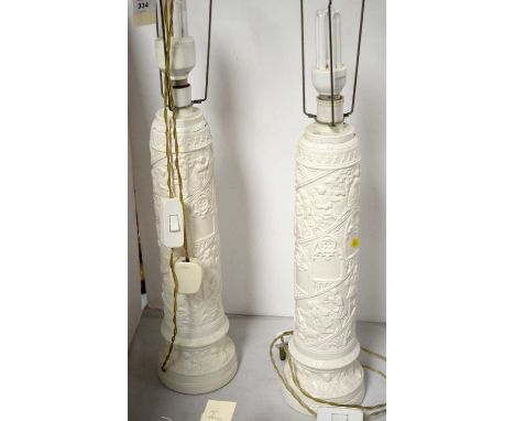 A pair of white painted table lamps, decorated with figural scenes in relief.